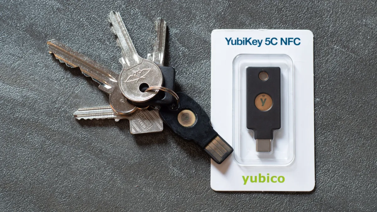 A security key attached to ordinary metal keys beside a packaged YubiKey 5C NFC on a grey surface.