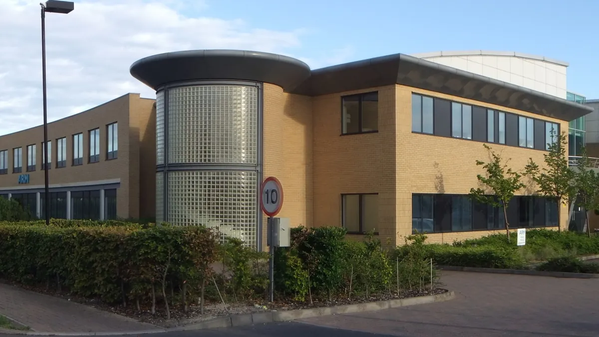 A brick Arm office building in Cambridge with a curved glass-block stairwell and landscaped grounds.