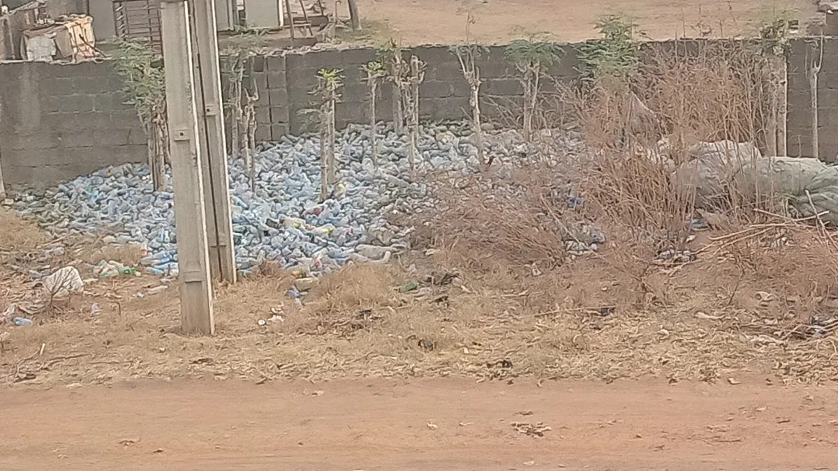 Discarded plastic bottles collected in piles beside a wall and sacks in an outdoor area.