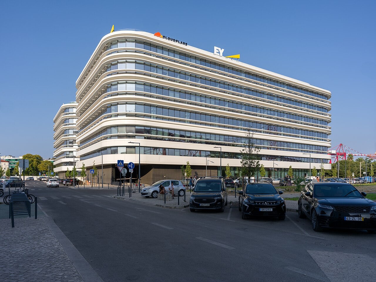 Curved glass and white exterior of an office complex in Alcântara, Lisbon, photographed beneath a blue sky.