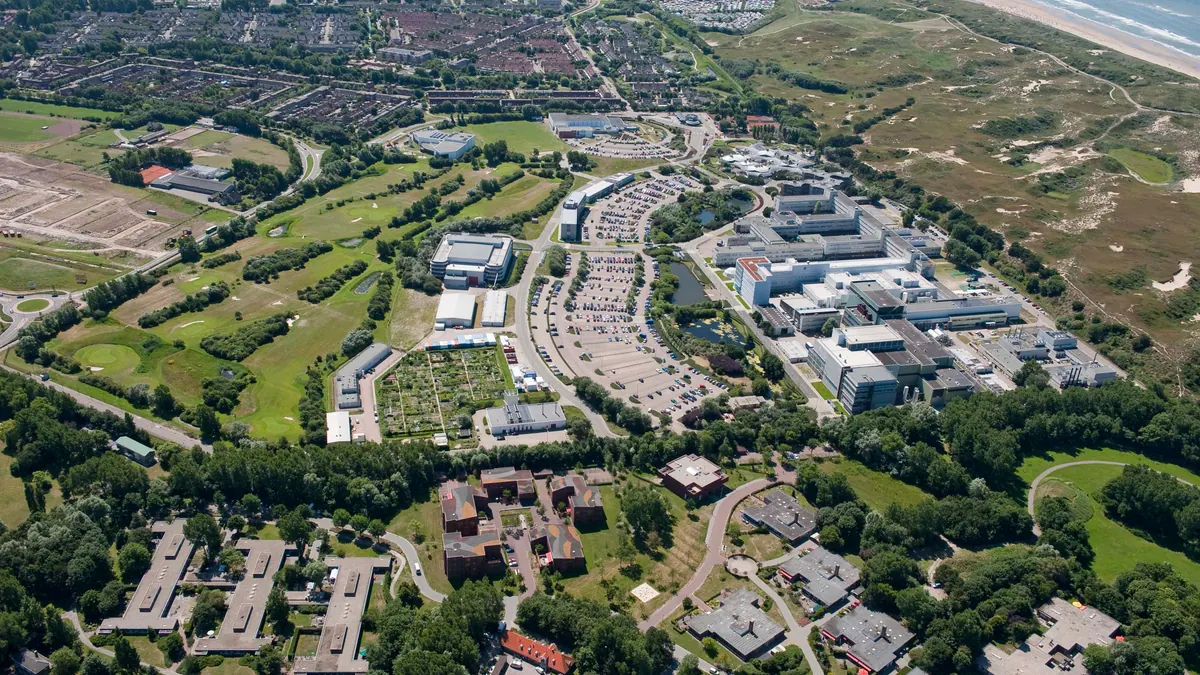 Aerial view of ESA's ESTEC campus, with laboratories, trees and the nearby Dutch coast.