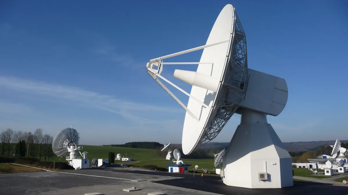 A large white satellite-navigation test dish at Redu stands against a blue sky, with smaller antennas in the background.