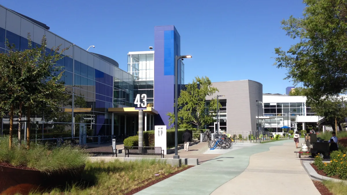 Googleplex Building 43 beside a landscaped campus path, with bicycles and glass-fronted offices under a clear blue sky.