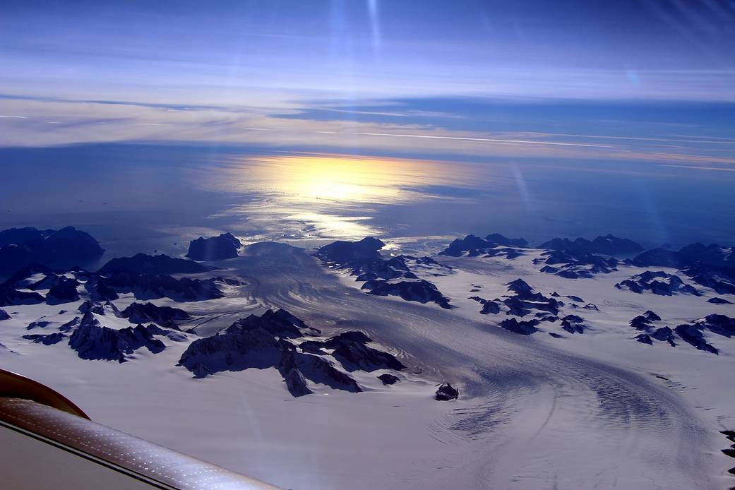 An aerial photograph of Greenland’s Steenstrup Glacier, with sunlight on the Denmark Strait beyond the glacier.