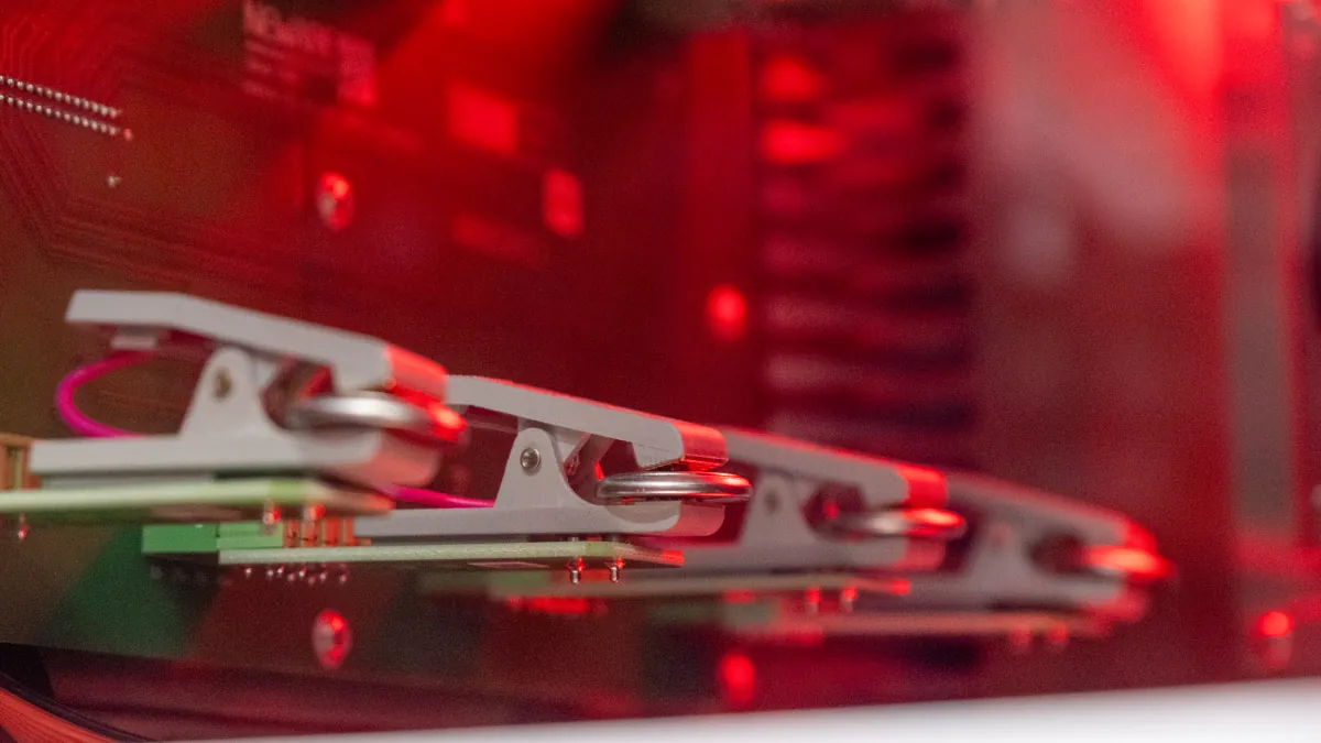 Small round coin cells held in a row of laboratory clamps under red lighting.