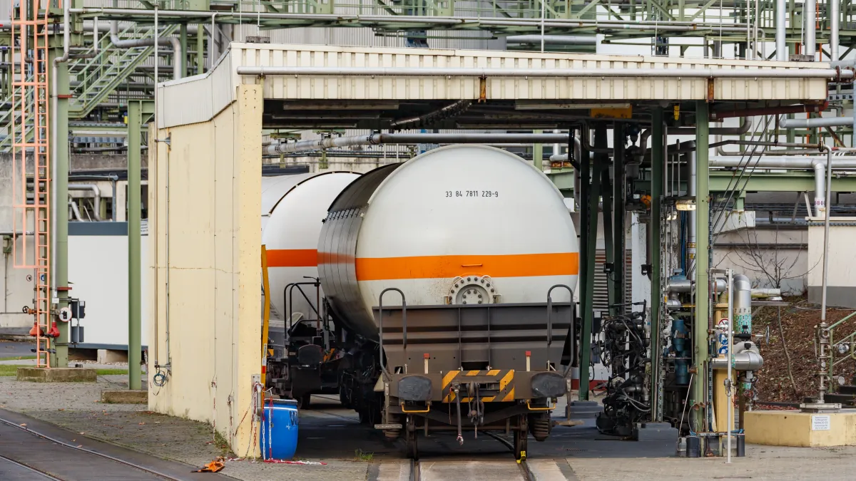 A white ammonia railway tank wagon with an orange stripe beside pipes at a covered industrial unloading station.