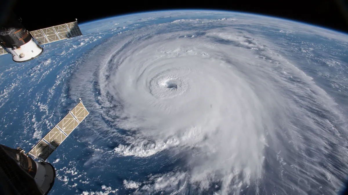 The eye and swirling white cloud bands of Hurricane Florence over the Atlantic, with spacecraft hardware at the left edge.