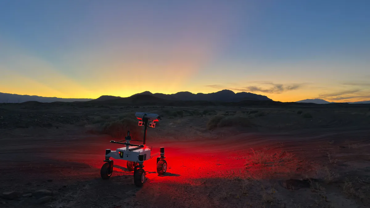 NASA JPL's four-wheel ERNEST rover driving across the Colorado Desert at dusk with red lights illuminating the ground.