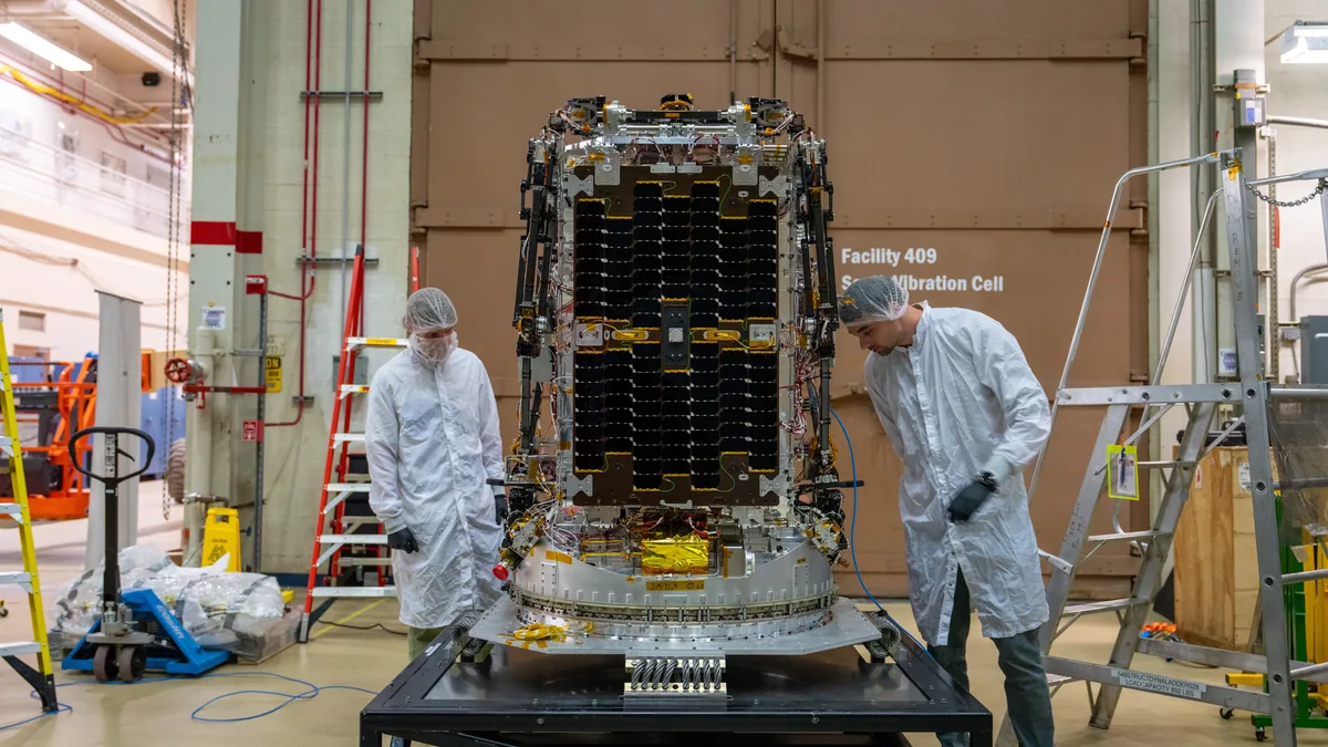 Two engineers in clean suits inspect the LINK spacecraft in a NASA test facility.