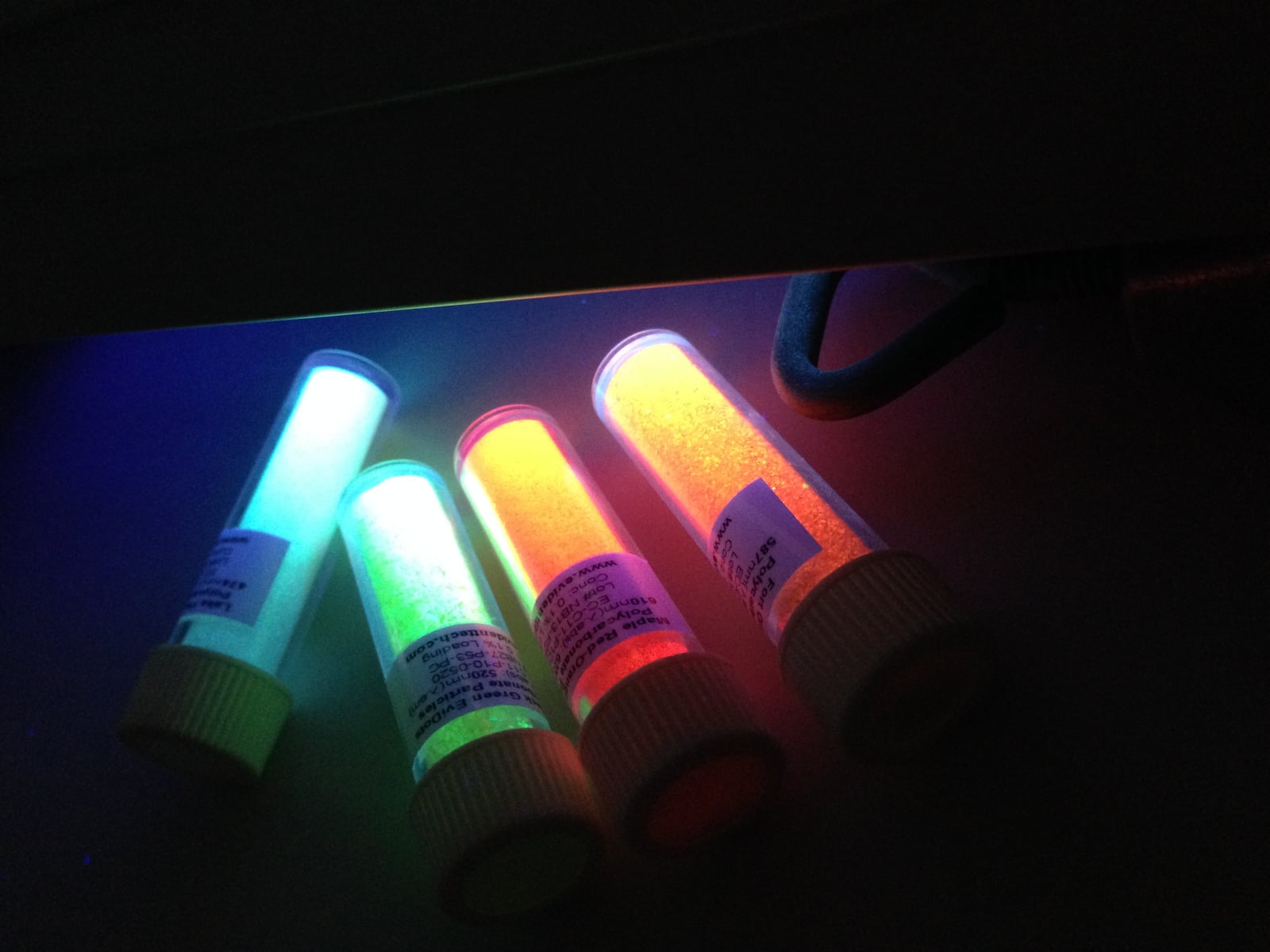 Archive photograph of quantum-dot samples glowing different colors under ultraviolet light.