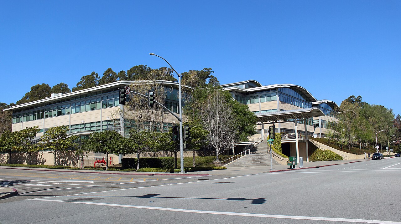 A curved office building at YouTube’s San Bruno campus, behind a lawn and trees.